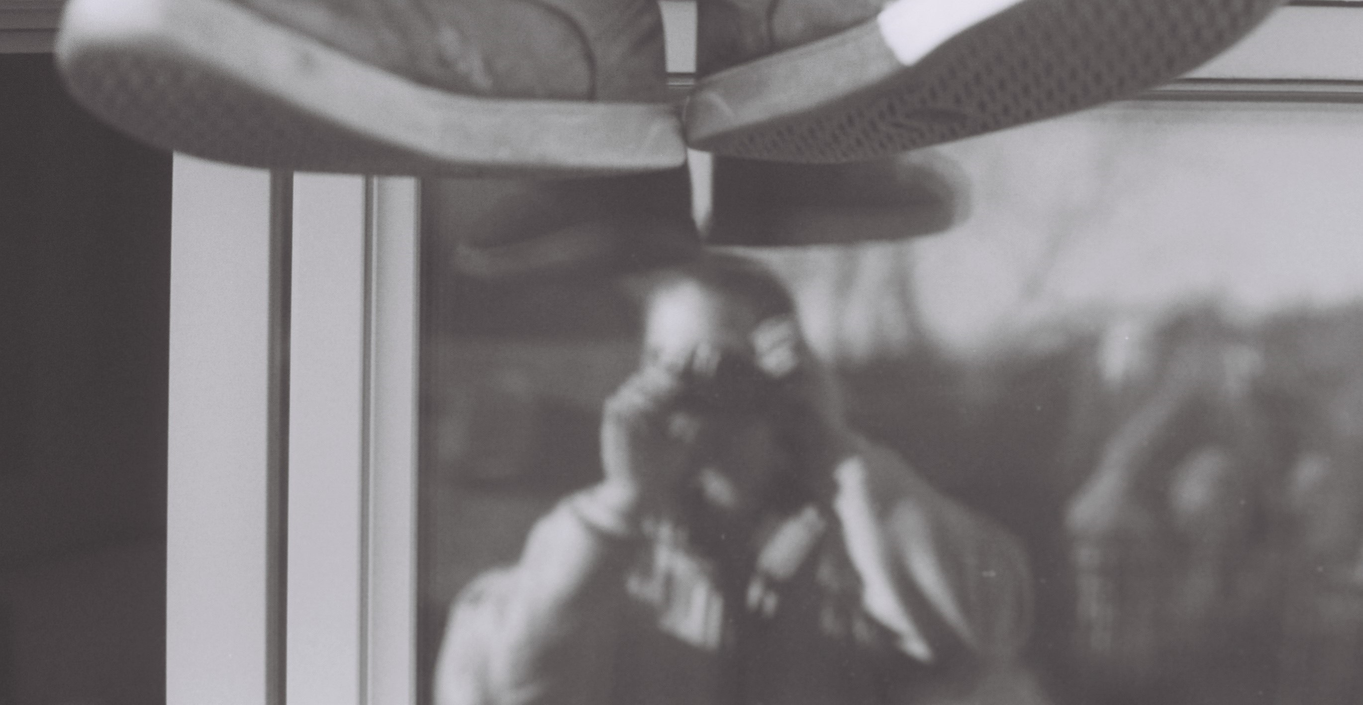 Kevin Blum reflected in a window while taking a photograph, with a pair of shoes overhead